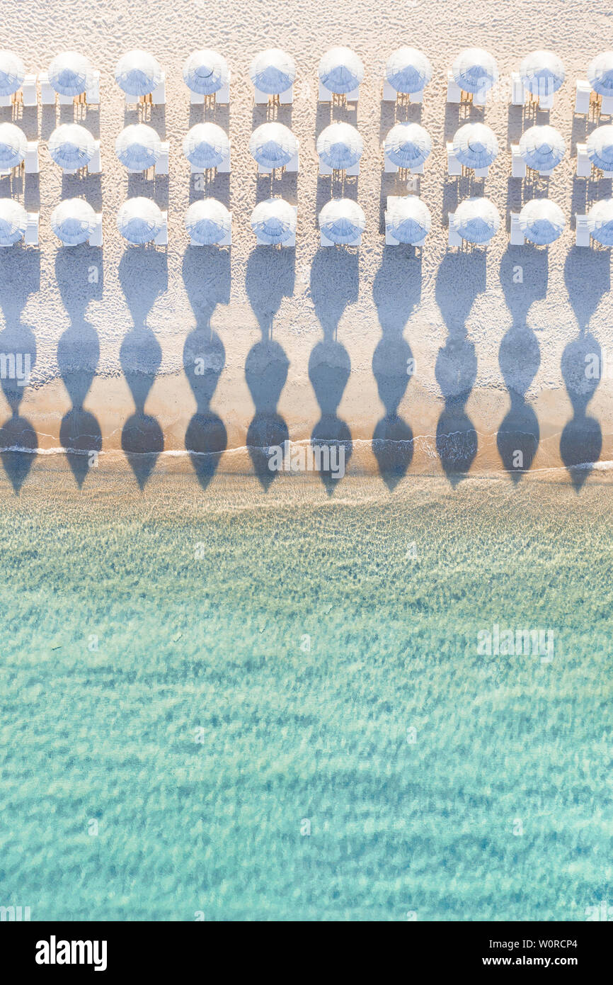 Ansicht von oben, atemberaubenden Blick auf eine erstaunliche leeren weißen Strand mit weißen Sonnenschirmen und türkisklares Wasser während des Sonnenuntergangs. Stockfoto