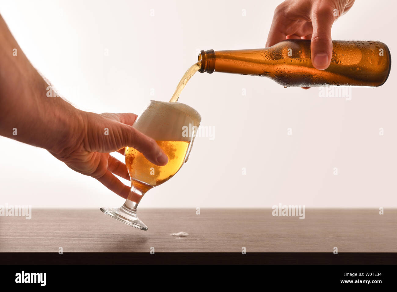 Hände füllen ein Bier Glas aus einer Glasflasche auf einer hölzernen Bar isoliert weiß. Horizontale Komposition. Vorderansicht. Stockfoto