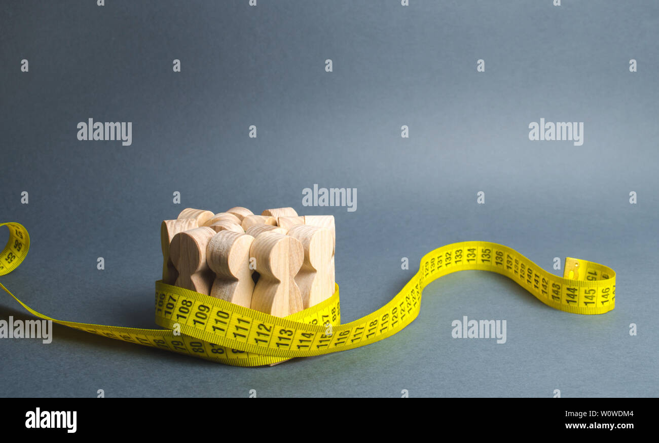 Eine Masse von Holzfiguren durch Maßband gegriffen wird. Sozialwissenschaften. Förderung der Ideen für Gewichtsverlust, Lifestyle. Informationen Statistiken, measureme Stockfoto