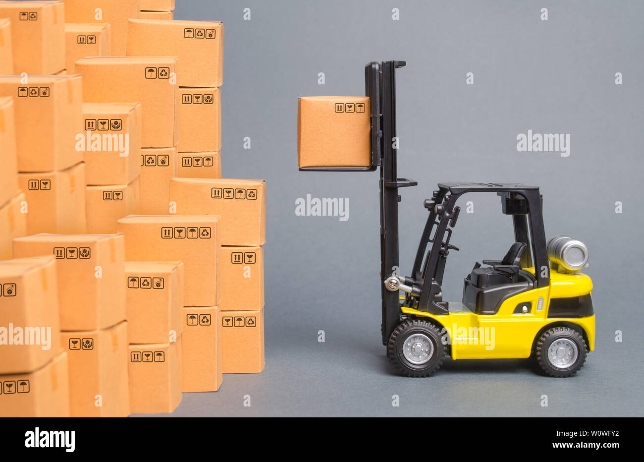 Gelbe Gabelstapler hebt eine Box auf einem Stapel von Kisten. Service Lagerung von Waren in einem Lagerhaus, Lieferung und Transport. Fracht und Lieferung Stockfoto