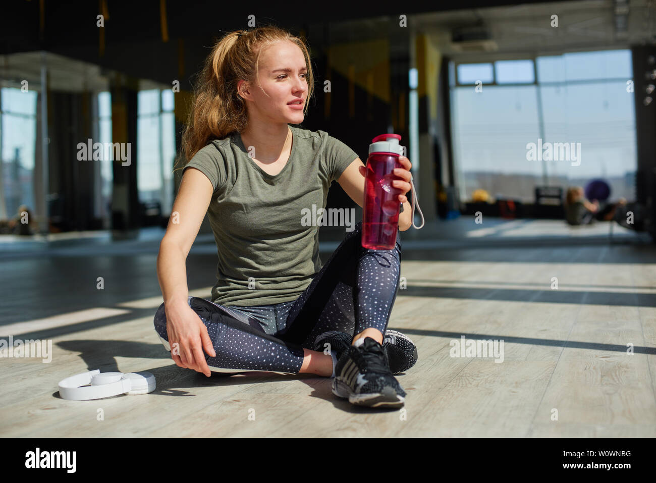 Mädchen in Ihrem Fitnessstudio Verschleiß sitzt auf dem Boden und trinken Wasser aus dem rosa Flasche. Stockfoto