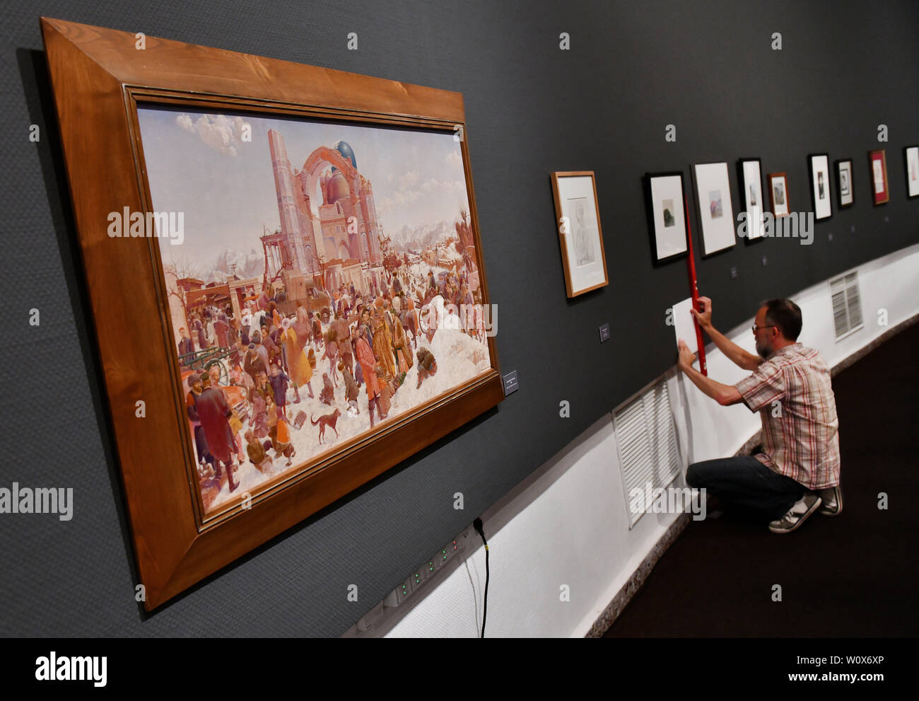 Bad Frankenhausen, Deutschland. 28 Juni, 2019. Ein Mitarbeiter der Panorama Museum hängt ein kleines Schild, ein Bild von dem Maler Werner Tübke, auf der linken das Bild "Bauernmarkt in Samarkand" von 1963. Die Ausstellung "Unter fremden Menschen" mit Bildern von tübke im Panorama Museum ab 29.06.2019 bis 03.11. 2019. Credit: Frank Mai/dpa-zentralbild/ZB - Nur für die Verwendung in Einklang mit vertraglichen Vereinbarung/dpa/Alamy leben Nachrichten Stockfoto