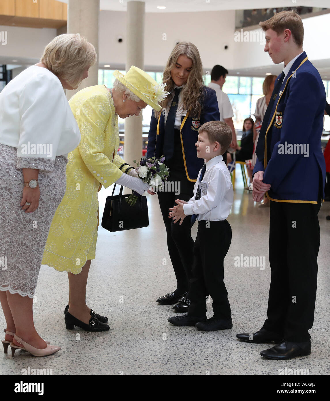 Königin Elizabeth II. Erhält ein sträußchen Blumen von Archie Wilson neben Elise McCormick und Cameron MacIndoe durch Schulleiterin Linda Park bei einem Besuch in Greenfaulds High School im Westen von Cumbernauld beobachtet. Stockfoto