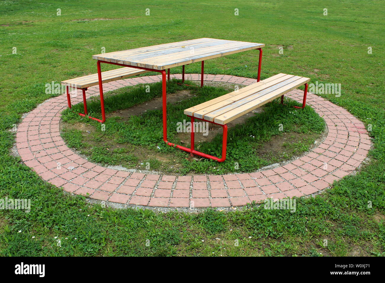 Öffentlicher Park Tisch mit zwei Bänken aus verfallenen Holz und Metall mit dekorativen Steine und ungeschnittenes Gras umgeben angeschlossen Stockfoto
