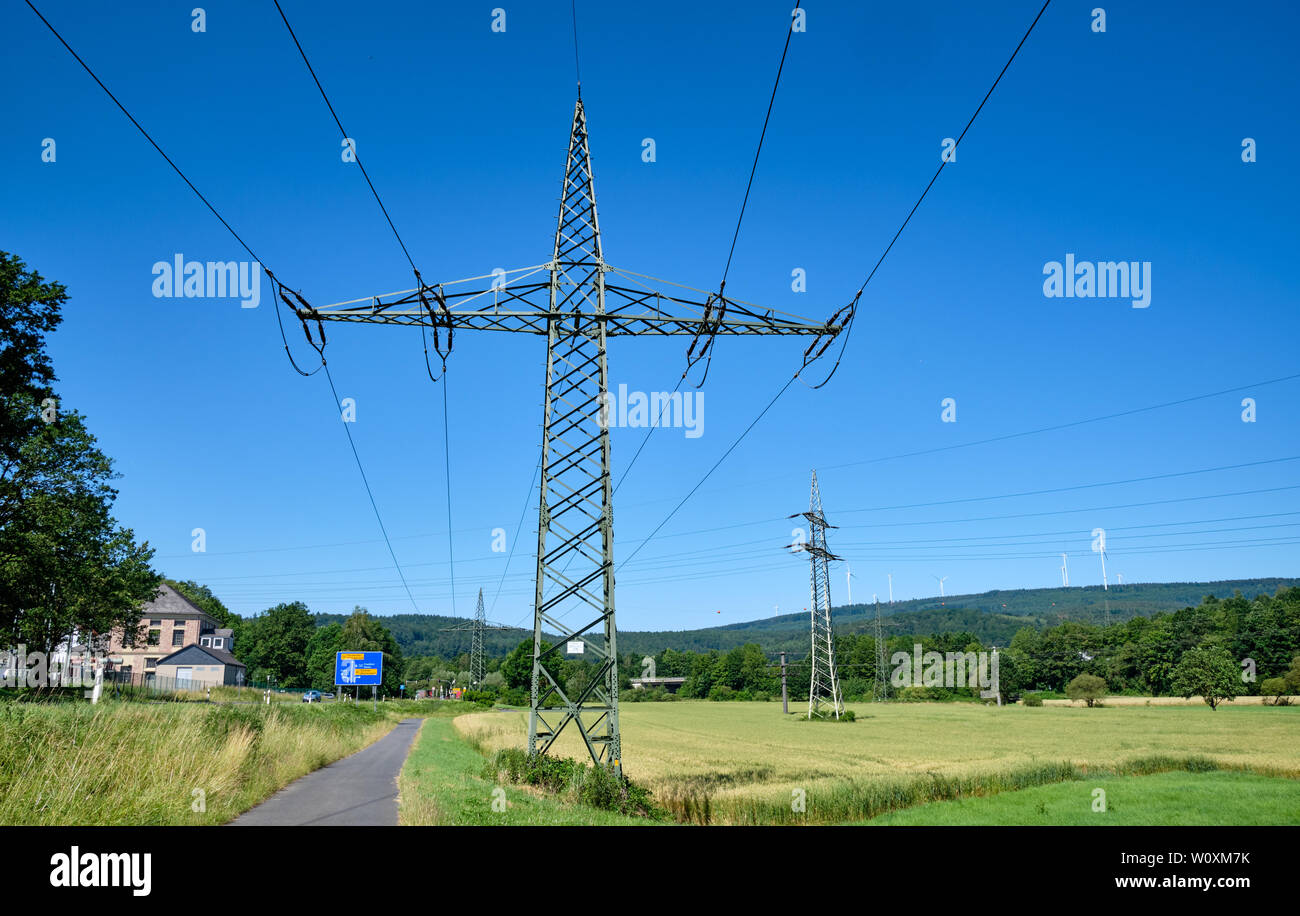 Zwei hohe strommasten gegen den blauen Himmel in einer wunderschönen ländlichen Sommer Landschaft mit Windkraftanlagen im Hintergrund Stockfoto