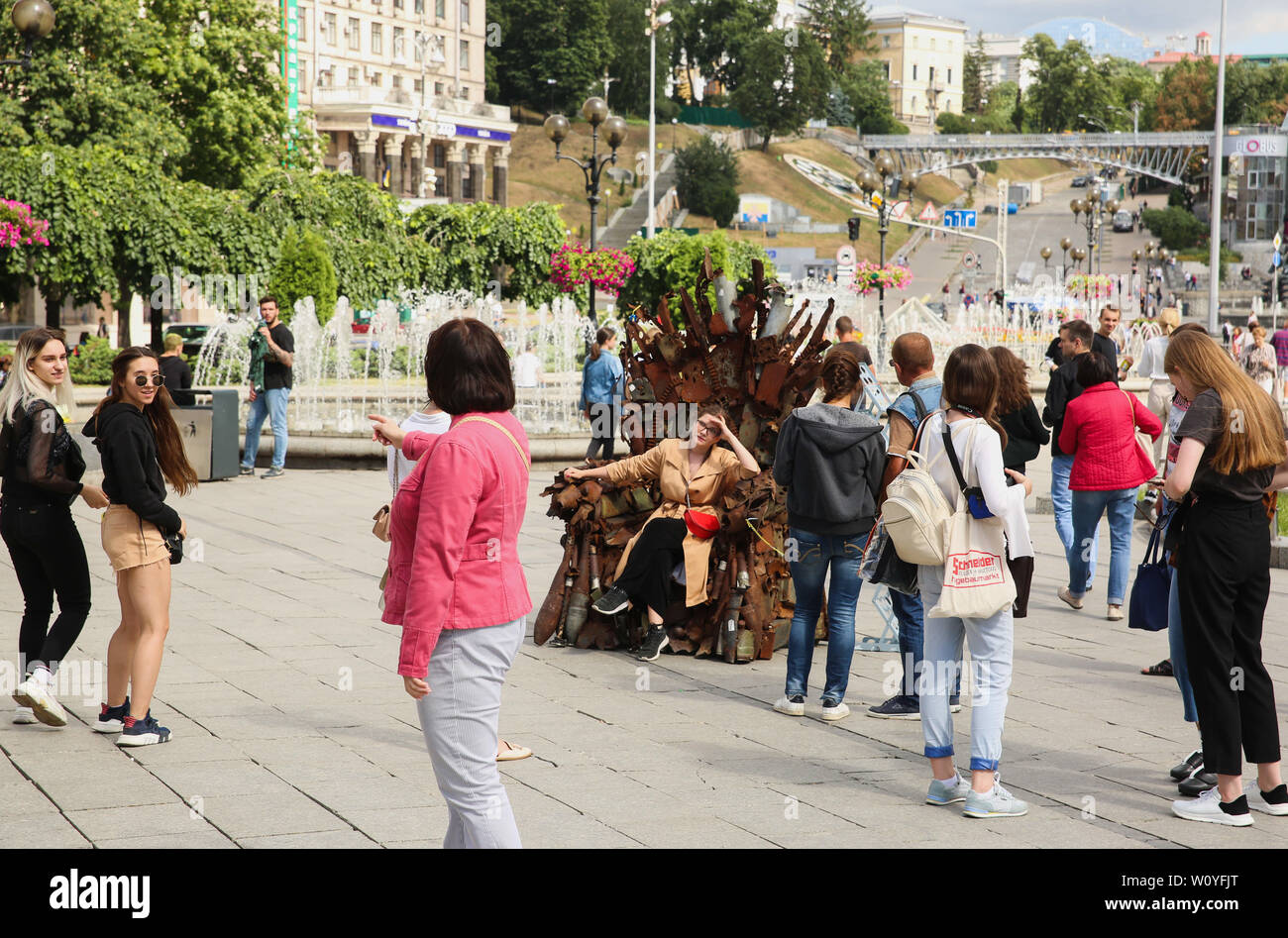 Kiew, Ukraine. 28 Juni, 2019. Menschen umgibt eine eiserne Thron auf dem Unabhängigkeitsplatz installiert, während ein Mädchen posiert für ein Foto in Kiew, Ukraine, 28. Juni 2019. "Der Eiserne Thron des Ostens'' durch die Armee freiwillige Denys Bushtets von MBT aktive Rüstung, Wrack, Fahrzeuge, Schutt Patrone Riemen, Raketen und Kolben war in der ukrainischen Hauptstadt ausgesetzt sind Bewohner der friedlichen Stadt des Krieges zu erinnern. Credit: sergii Kharchenko/ZUMA Draht/Alamy leben Nachrichten Stockfoto