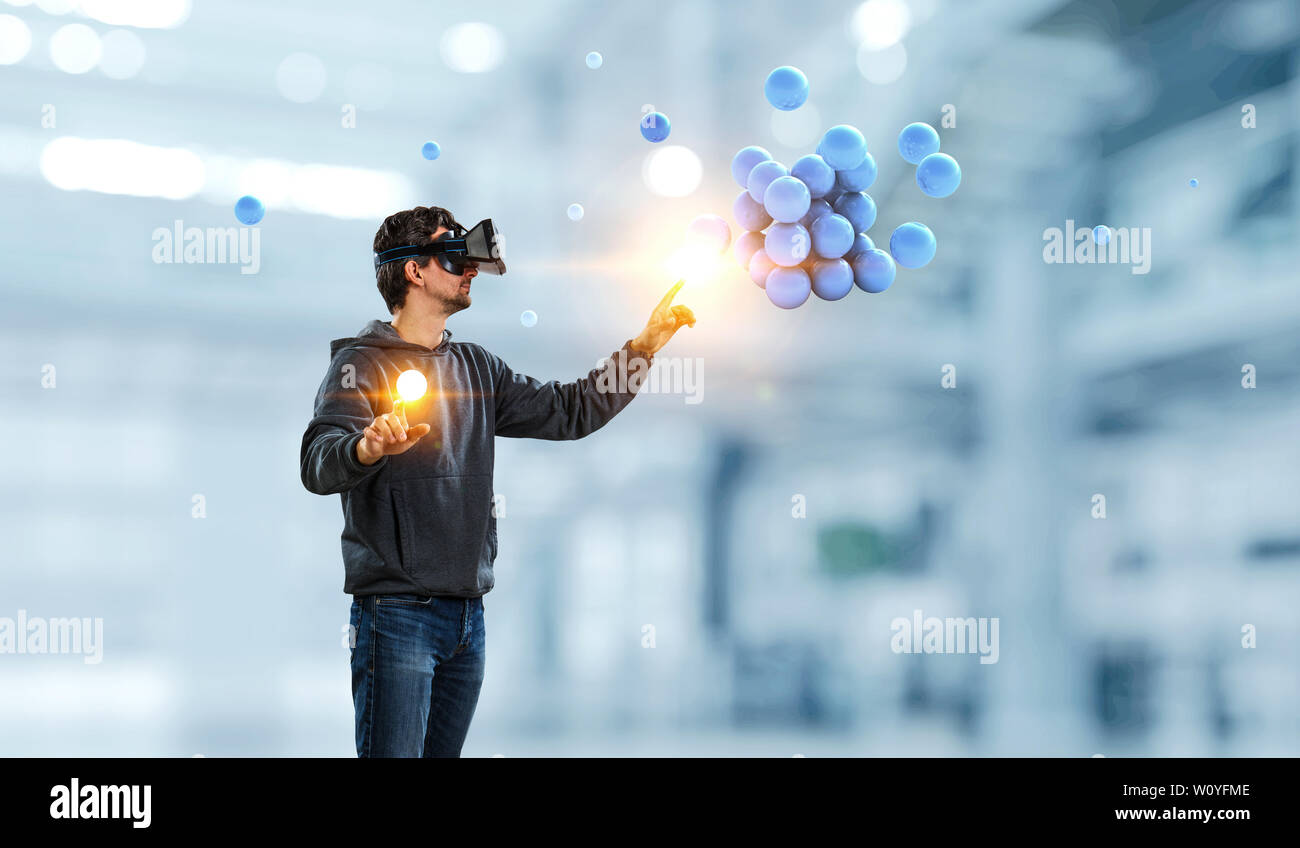 Junger Mann in VR-Headset mit abstrakten Haufen Sphären. Mixed Media Stockfoto