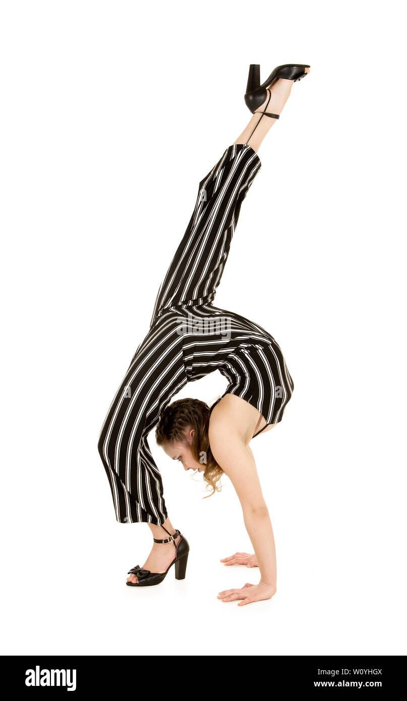 Eine junge, lächelnde Frau im gestreiften Anzug führt gymnastische und akrobatische Übungen durch. Studio-Aufnahmen auf weißem Hintergrund. Stockfoto