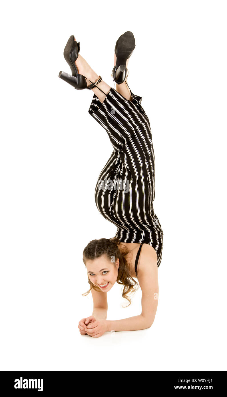 Eine junge, lächelnde Frau im gestreiften Anzug führt gymnastische und akrobatische Übungen durch. Studio-Aufnahmen auf weißem Hintergrund. Stockfoto