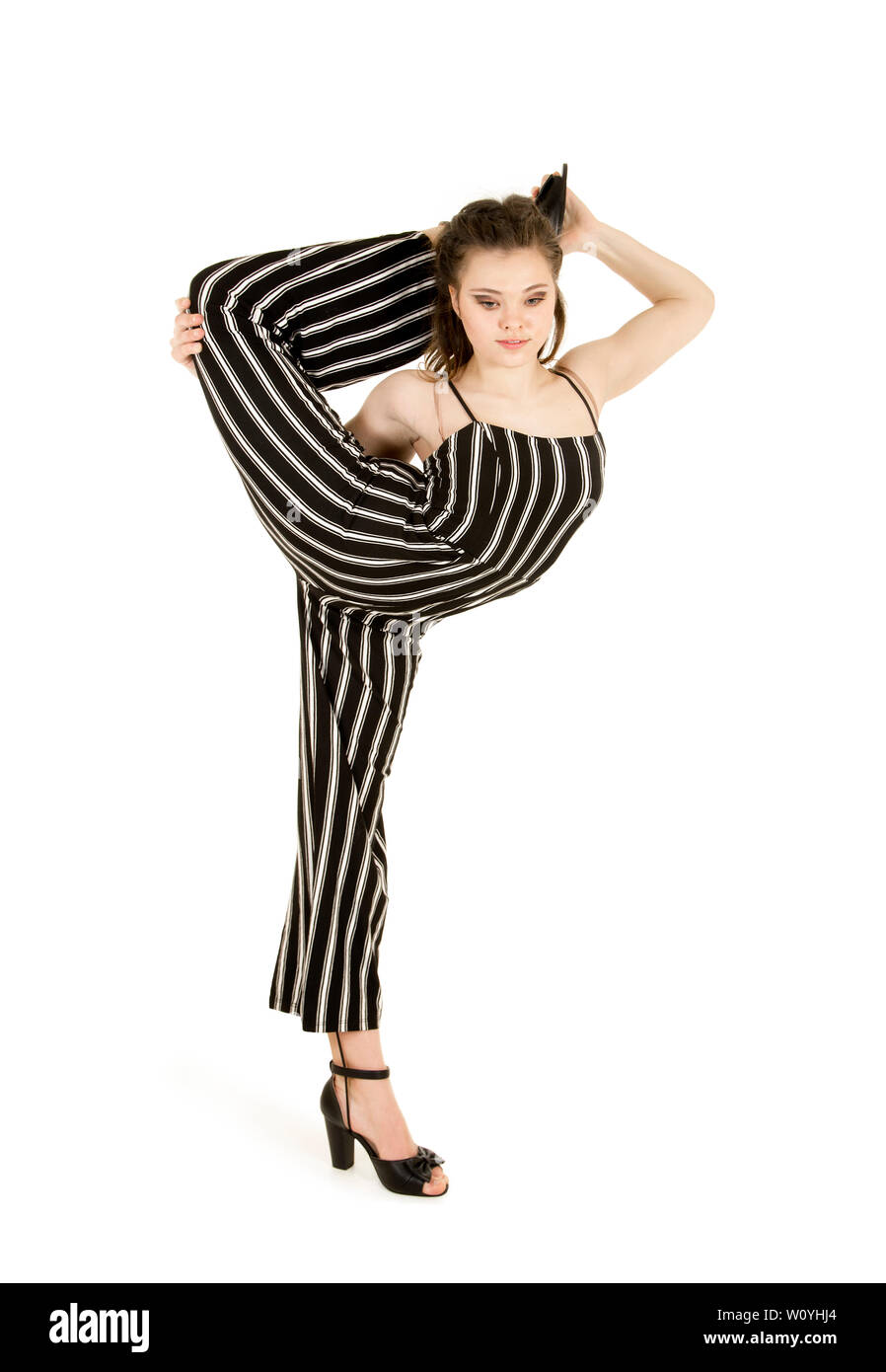Eine junge, lächelnde Frau im gestreiften Anzug führt gymnastische und akrobatische Übungen durch. Studio-Aufnahmen auf weißem Hintergrund. Stockfoto
