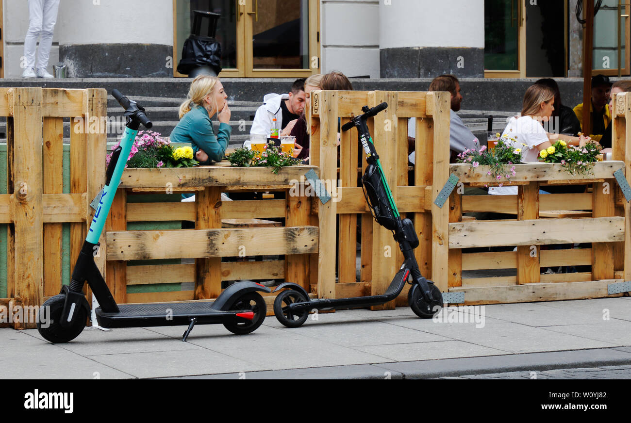 Oslo, Norwegen - 20. Juni 2019: Geparkte elektrisch angetriebene push Roller vor ein Restaurant im Freien mit Europa Paletten eingezäunt. Stockfoto