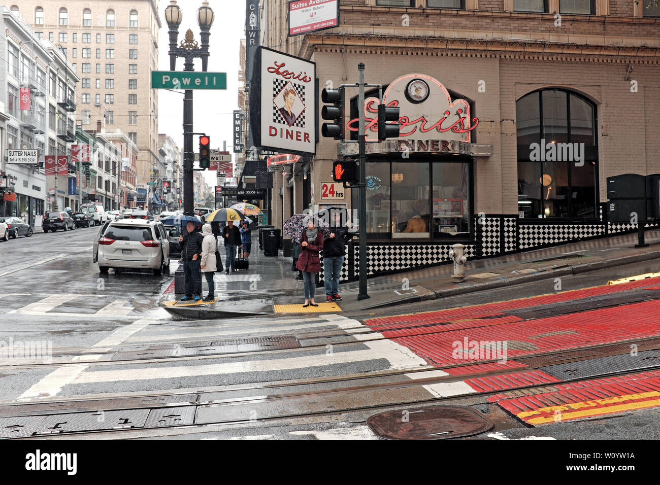 Ein Paar hält Regenschirme vor Loris Diner, während sie bei einem Regensturm in San Francisco, Kalifornien, USA die Powell Street überqueren. Stockfoto