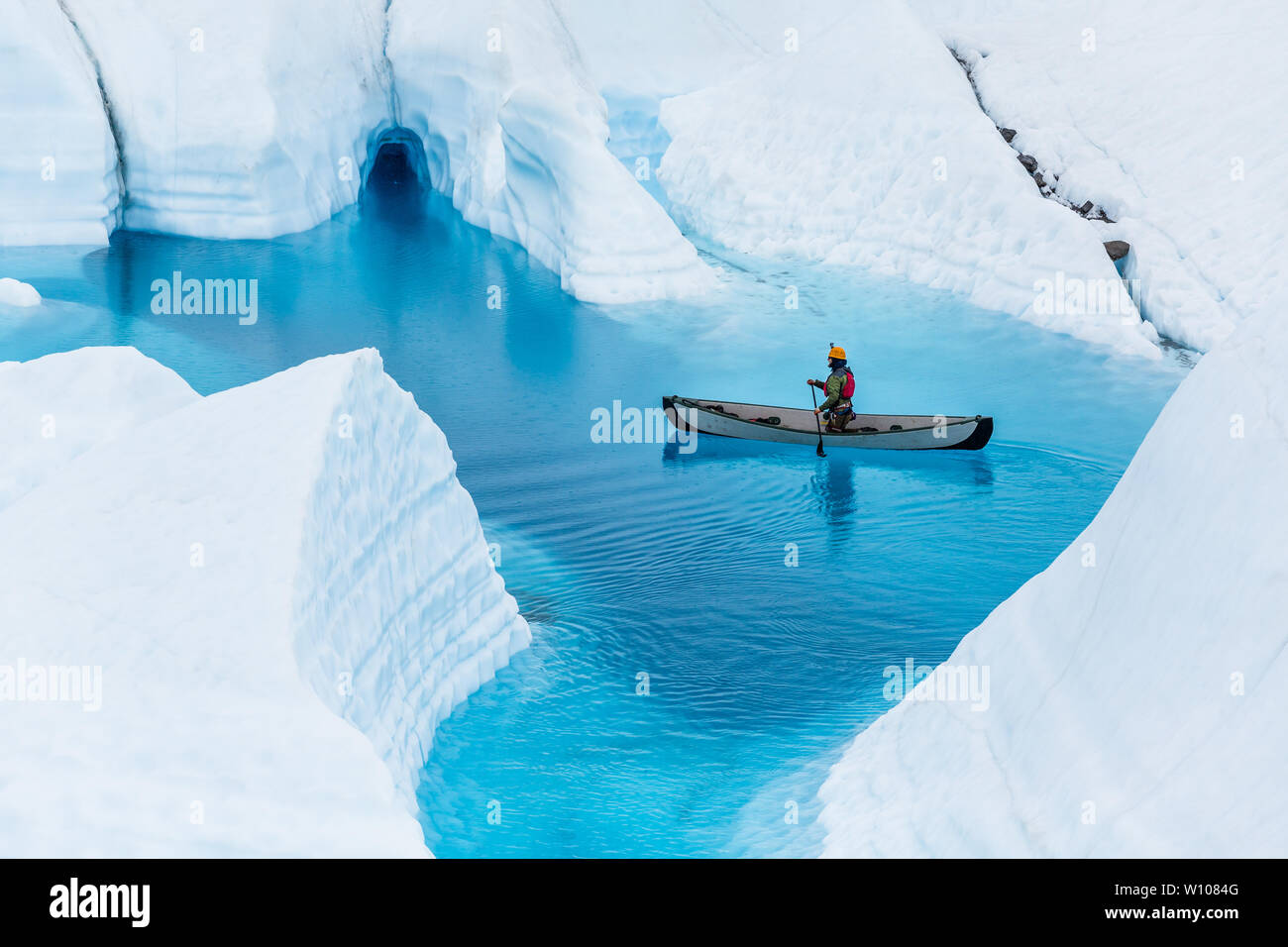 Mann auf einem Kanu schwebt über einem überfluteten Eishöhle in einem tiefen blauen Pool während in Alaska, regnete Stockfoto