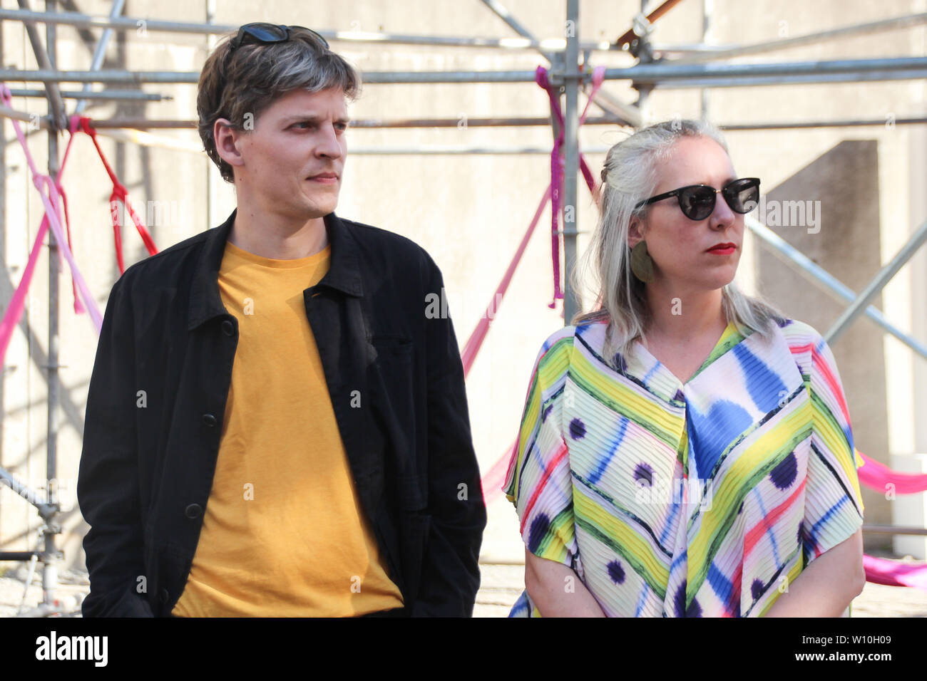 New York, USA. 27 Juni, 2019. Die deutsch-mexikanische Architekt duo Pedro & Juana (Mecky Reuss (l) und Ana Paula Ruiz Galindo) steht vor dem MoMA PS1 Museum. Die Architekten haben einen urbanen Dschungel - mit Hängematten und einem künstlichen Wasserfall gebaut. Eine kreisförmige Gerüst etwa zwölf Meter hoch mit einem Durchmesser von fast 30 Metern ist mit Jungle Motiven bedruckt. Es wird auf der Anzeige, bis 2. September auf die Außenwände der äußeren Hof des Museums. Credit: Christina Horsten/dpa/Alamy leben Nachrichten Stockfoto