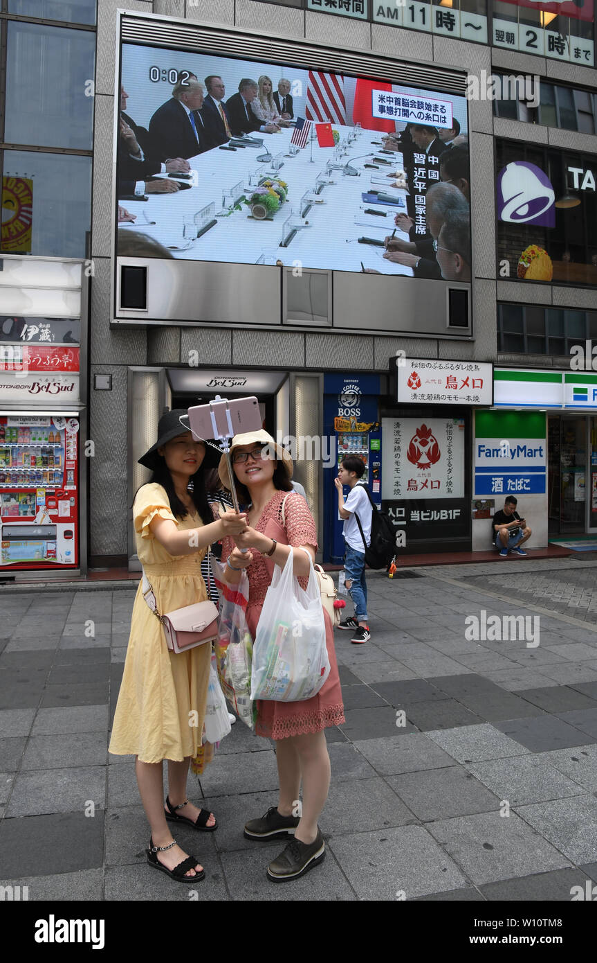 Osaka, Japan. 29 Juni, 2019. Zwei chinesische Touristen nehmen eine selfie Während ein aktuelles Update der G20-Treffen zwischen US-Präsident Donald Trump und der chinesische Präsident Xi Jinping war auf einem großen Bildschirm in Namba, Osaka Japan angekündigt. Am gleichen Tag Präsidenten, Premierminister und andere Führungskräfte aus der ganzen Welt Für den zweiten Tag des Osaka G20-Gipfel versammelt. Foto am Samstag, 29. Juni 2019 übernommen. Foto: Ramiro Agustin Vargas Tabares Credit: Ramiro Agustin Vargas Tabares/ZUMA Draht/Alamy leben Nachrichten Stockfoto