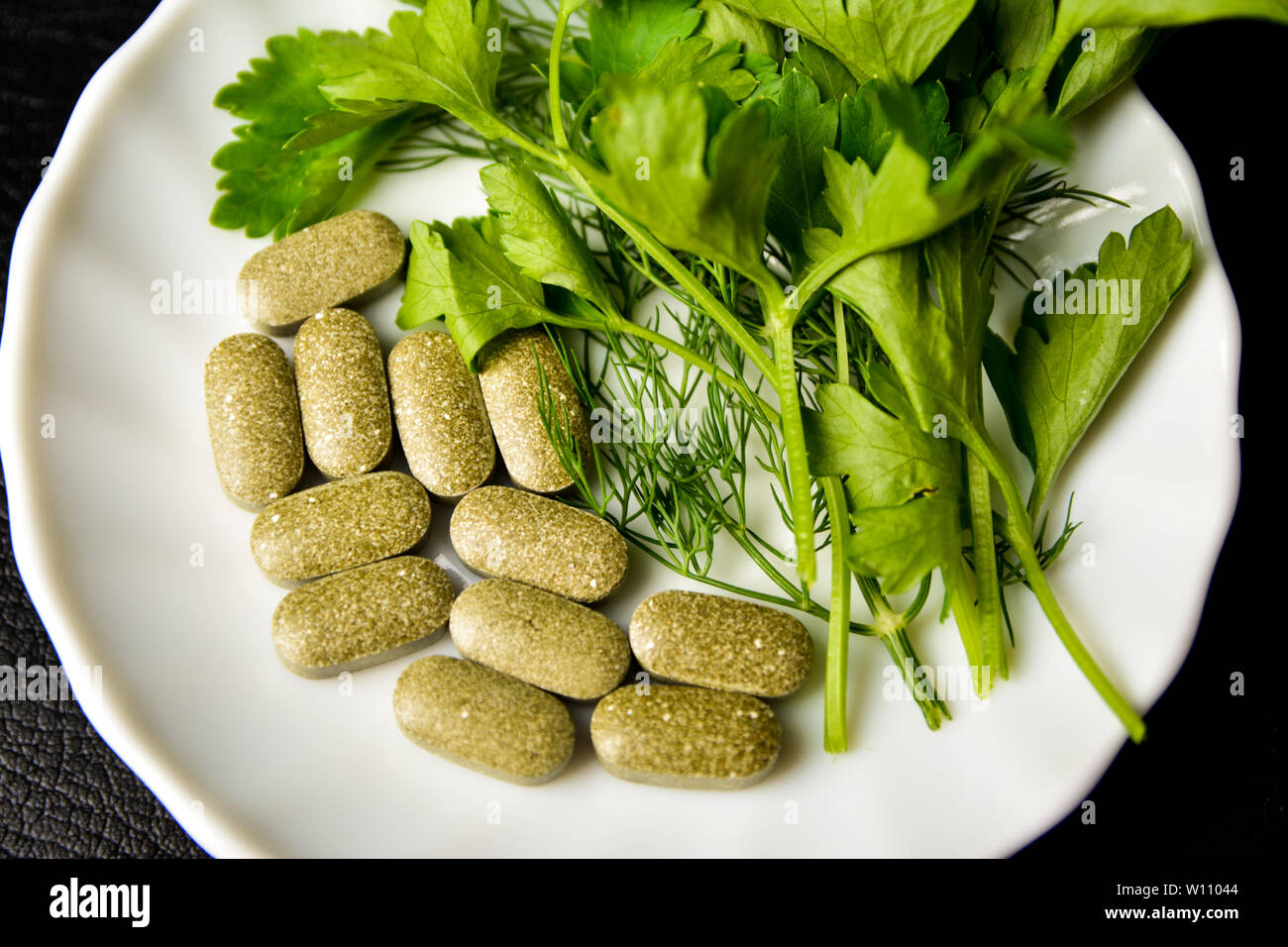 Gesunde Ernährung, alternative Essen, Petersilie in den Blättern und Tabletten auf einem weißen Teller. Stockfoto