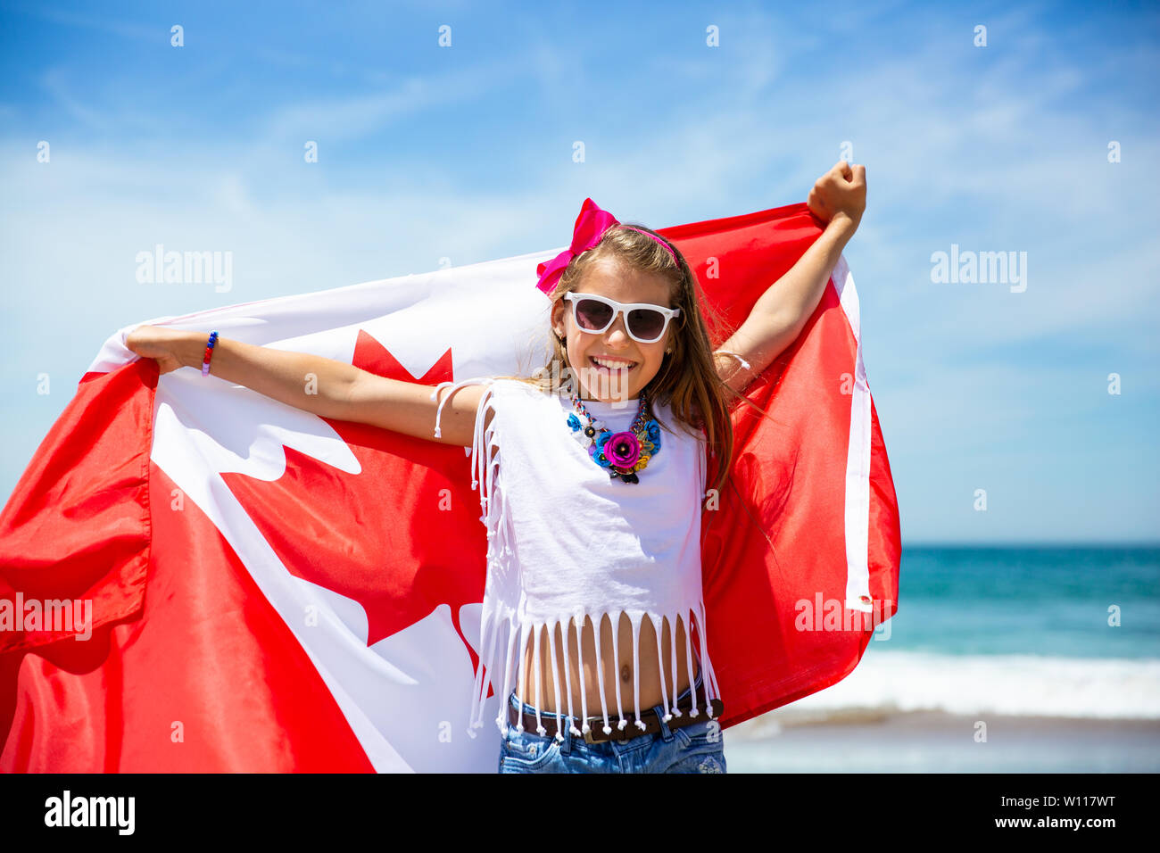 Happy kanadische Mädchen trägt flattern weiße rote Flagge von Kanada gegen den blauen Himmel und das Meer im Hintergrund. Kanadische Flagge ist ein Symbol der Freiheit, Freiheit Stockfoto