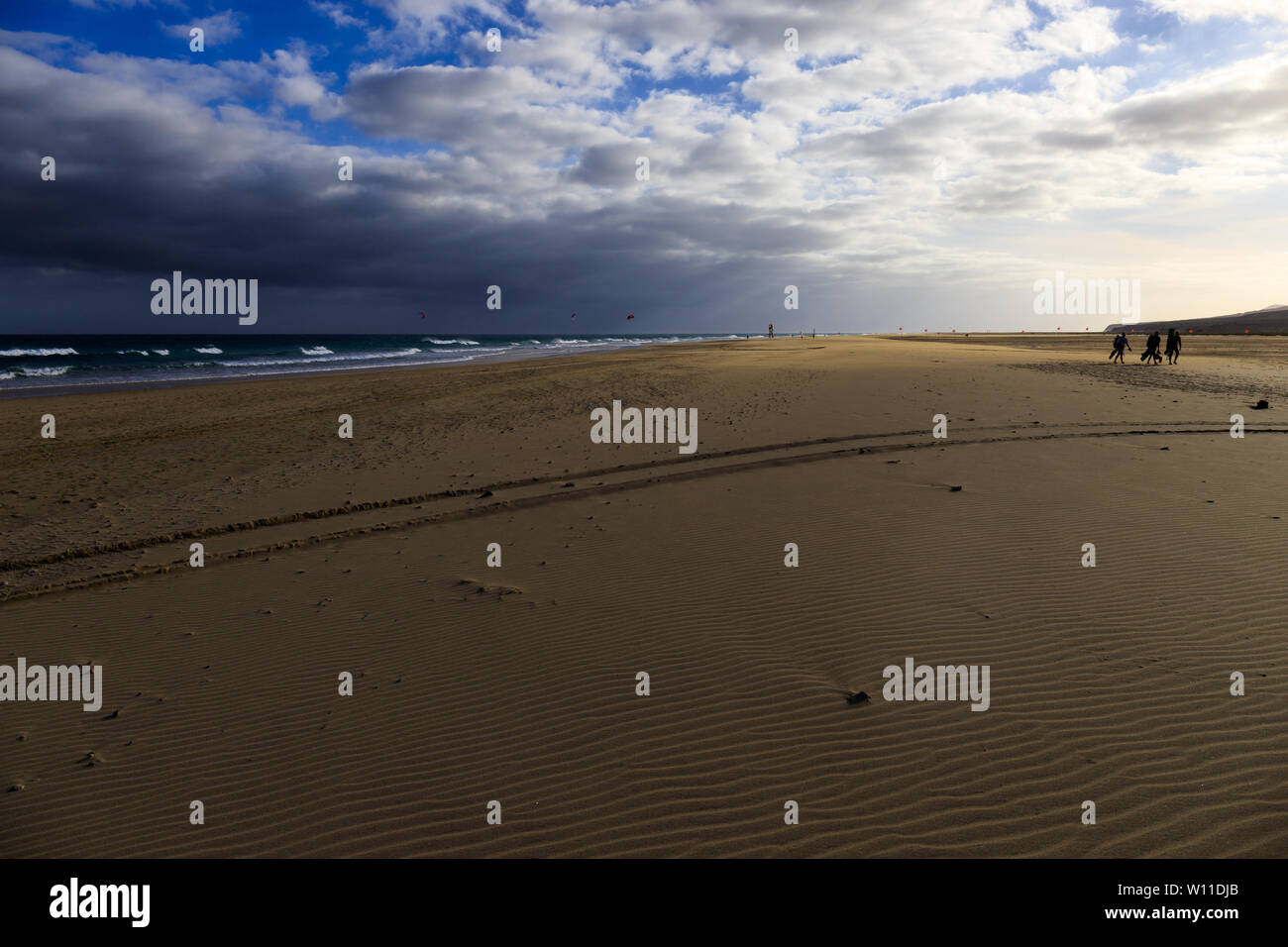 Schöne und windigen Strand bei Sonnenuntergang mit Menschen üben Kitesurfen in den Hintergrund und die Reifenspuren im Sand Stockfoto