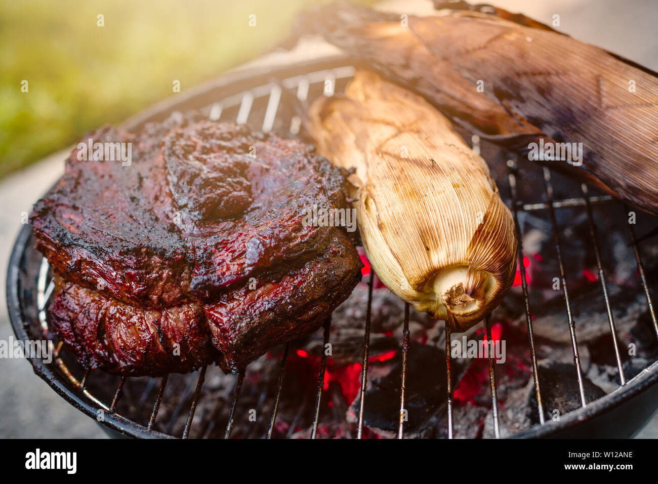 Eine große Rindfleisch Brustbein und Mais in der Schale gegrillt auf einem  kleinen Kohle Hibachi, Grill mit glühenden Kohlen unter mit einem  sonnenschliff Stockfotografie - Alamy