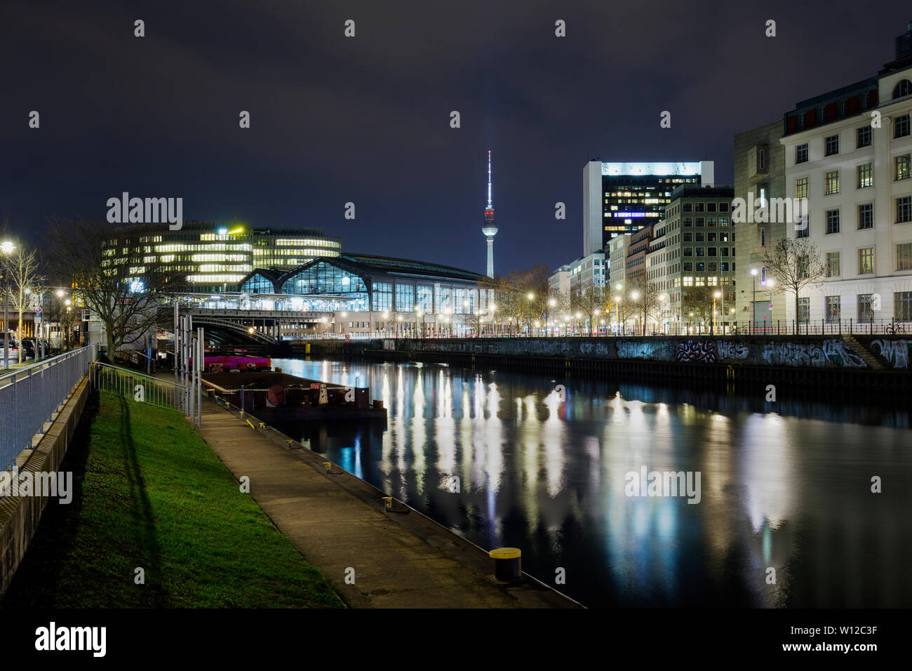 Leuchtet auf dem Bahnhof Friedrichsstraße und anderen Gebäuden, die von der Spree und Fernsehturm Fernsehturm in Berlin, Deutschland, in der Dämmerung. Stockfoto