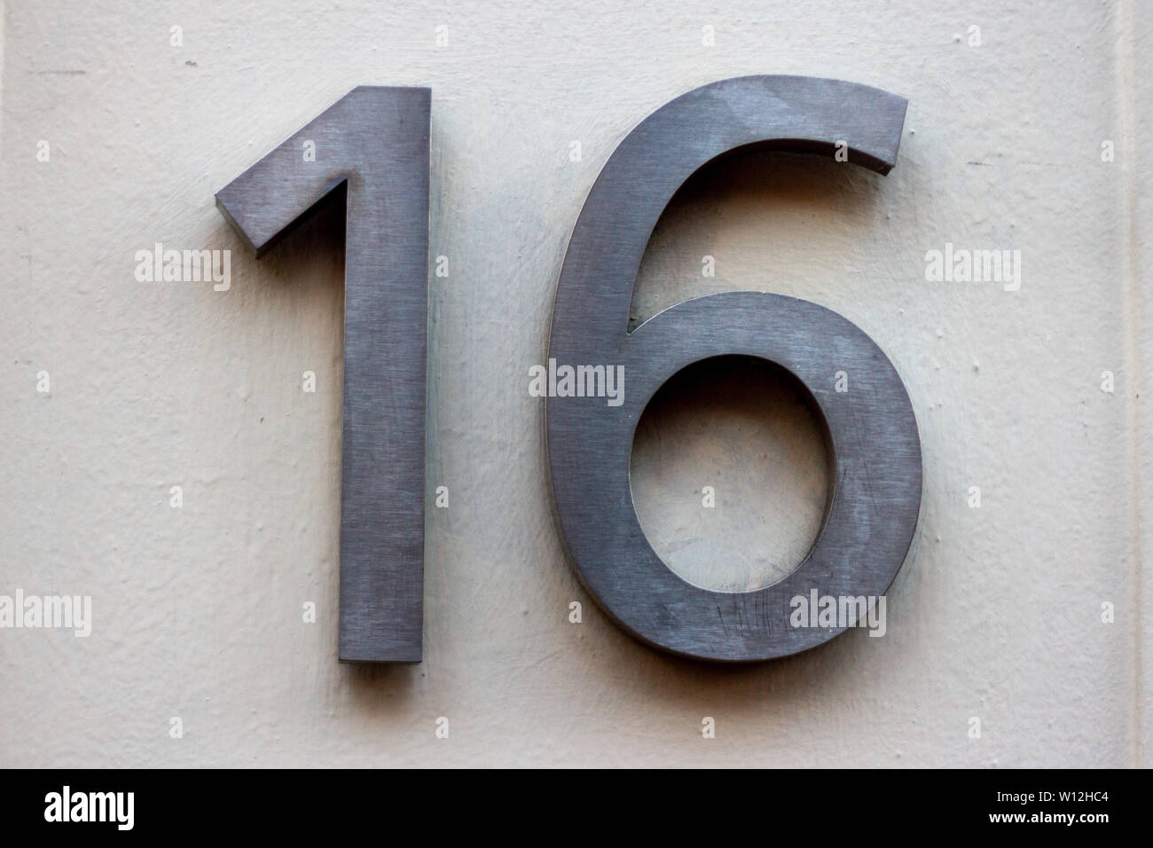 Haus Nummer 16 mit sechzehn in gebürstetem Chrom oder Edelstahl auf einer weißen Wand Stockfoto