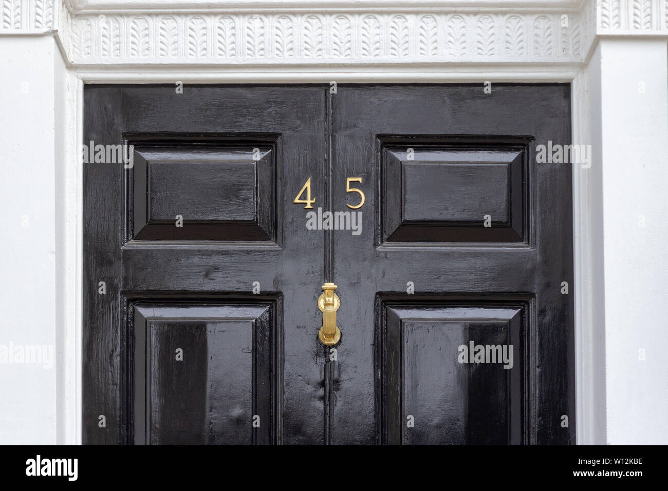 Haus Nummer 45 mit den vierzig - fünf in Metall Ziffern auf einem schwarz lackierten alte hölzerne Eingangstür mit geschnitzten weißen Stein Türrahmen Stockfoto