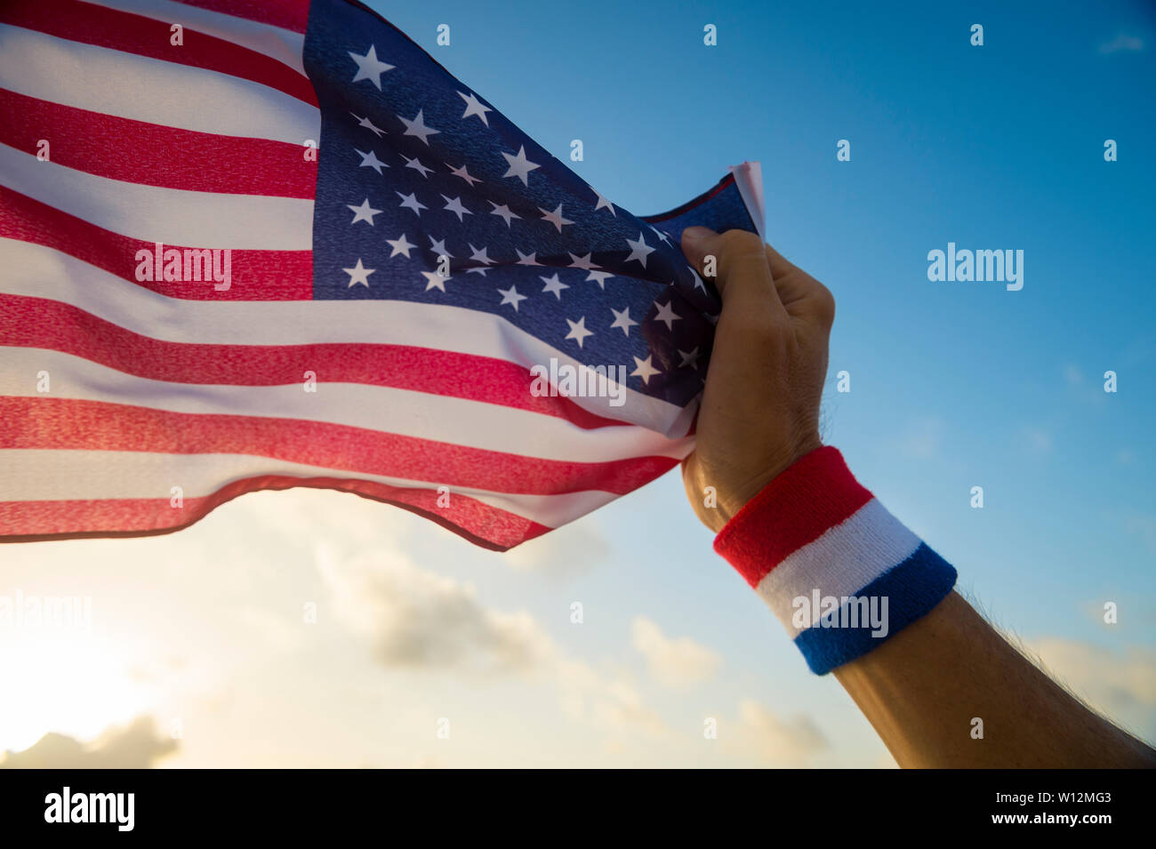 Patriotische hand mit USA rot, weiß und blau Armband Holding eine amerikanische Flagge schwenkten in goldenen sonnigen blauen Himmel Stockfoto