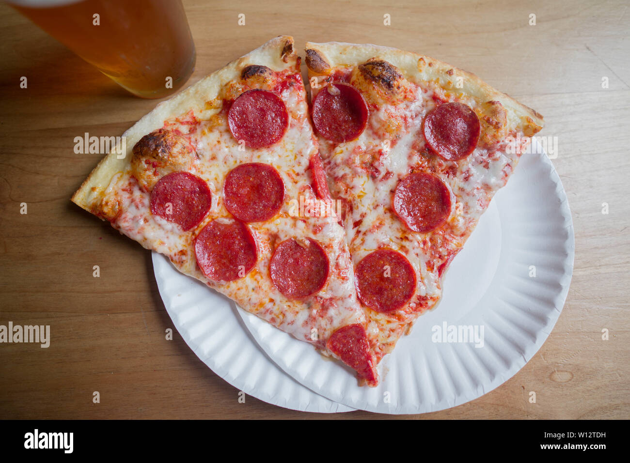 Zwei Scheiben Salami Pizza auf dem Teller mit einem Bier Stockfoto