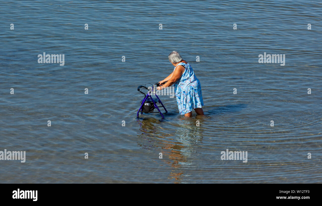 Ältere Dame geht mit Walker im Meer in den Morgen. Stockfoto