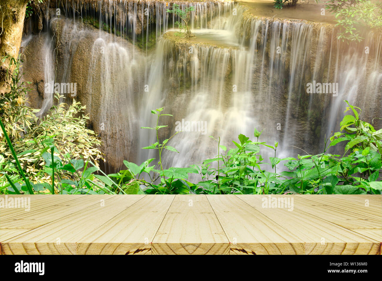 Leere Holz Tisch mit schönen landschaftlichen des Wasserfalls und grüne Blätter für erfrischende und entspannende Hintergrund. Stockfoto