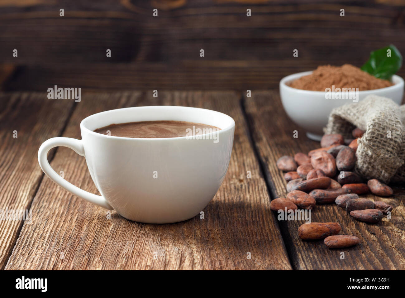 Kakao trinken in Weiß Becher, Kakaopulver und Kakaobohnen auf hölzernen Tisch. Stockfoto