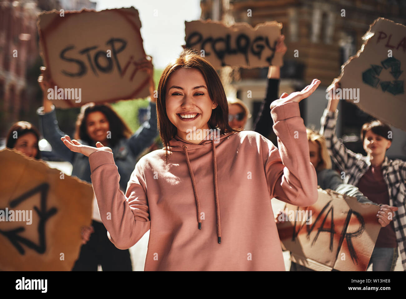 Wir lieben unseren Planeten. Glückliche junge Frau Gestik und lächelnd, während protestieren für Ökologie mit einer Gruppe von Aktivistinnen auf der Straße. Ökologie Konzept. Gruppe protestieren Stockfoto