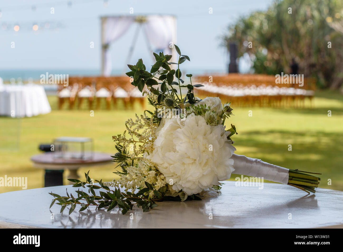 Wedding Bouquet mit weißen Pfingstrose und Rosen. Hochzeit arch und Stühle aus Holz für eine Zeremonie im Hintergrund. Tropische Hochzeit. Bali. Stockfoto