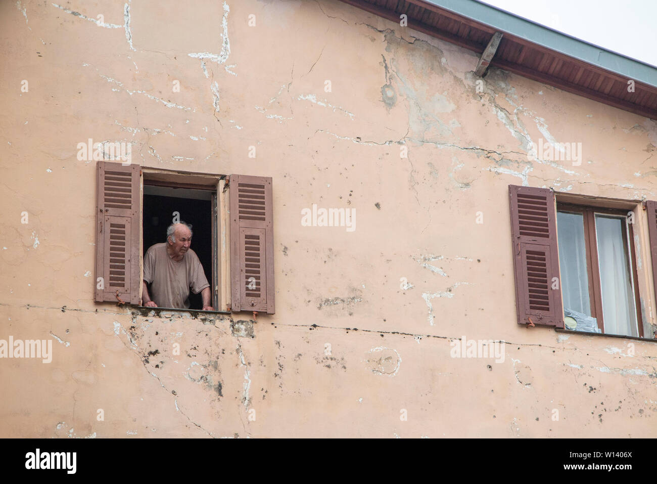 Ein alter Mann schaut aus seinem Fenster mit Fensterläden in Frankreich Stockfoto