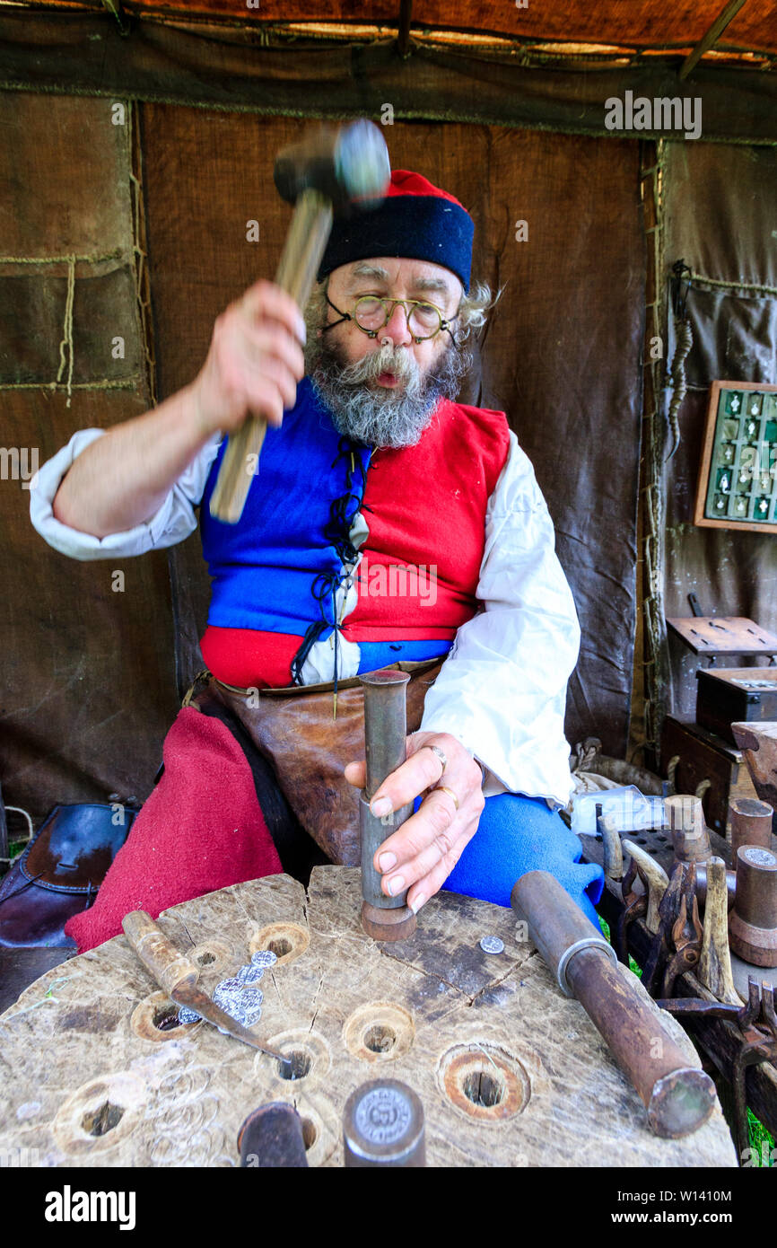 Mittelalter reenactment Event. Ältere Menschen, Metallarbeiter, mit buschigem Bart, sitzen an Werkbank, die Münzen mit einem Hammer und Holz geprägte Stempel. Stockfoto