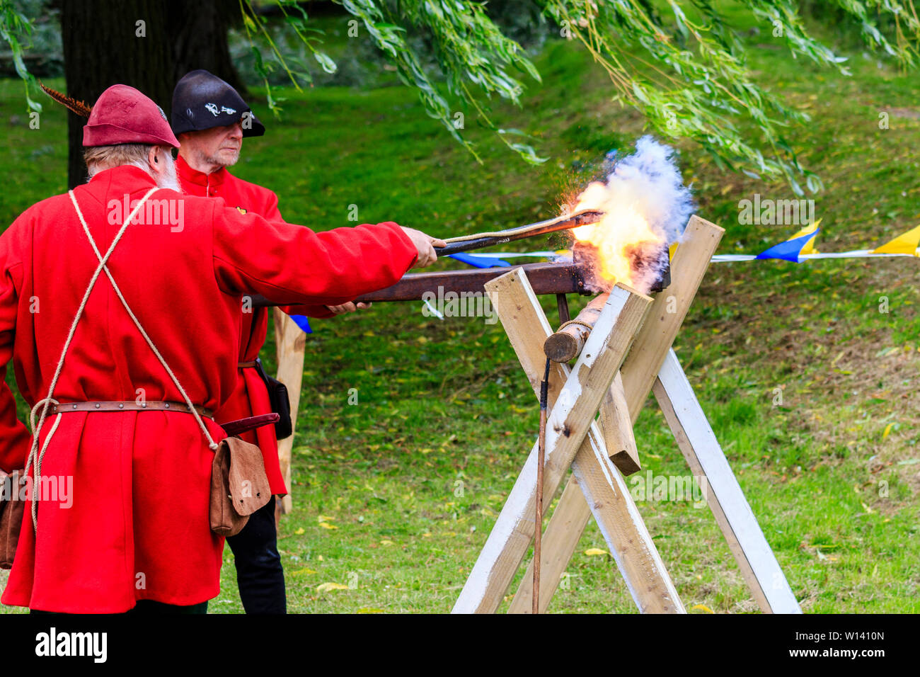 Mann gekleidet in mittelalterlichen Roten gunner Outfit und feuerte eine harquebus, arquebus, montiert auf einer Halterung. Rauch und Feuer. Mittelalterliche Re-enactment Veranstaltung. Stockfoto