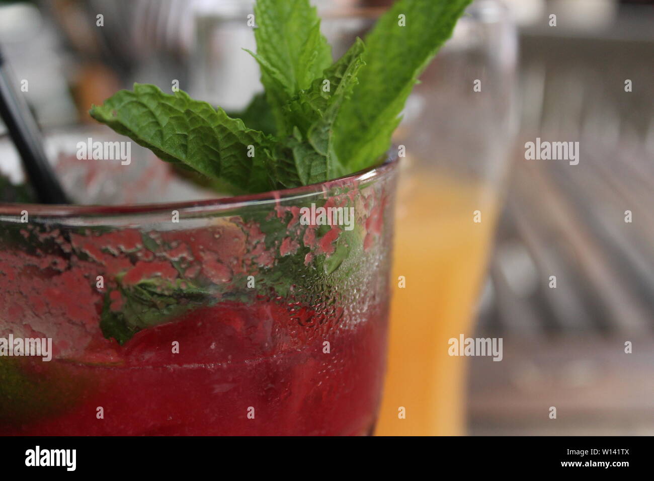 In der Nähe von Getränke Glas mit lila Cocktail und leaf Dekoration mit Orangensaft Glas dahinter, auf einem Tisch in einem Biergarten an einem sonnigen Tag Stockfoto