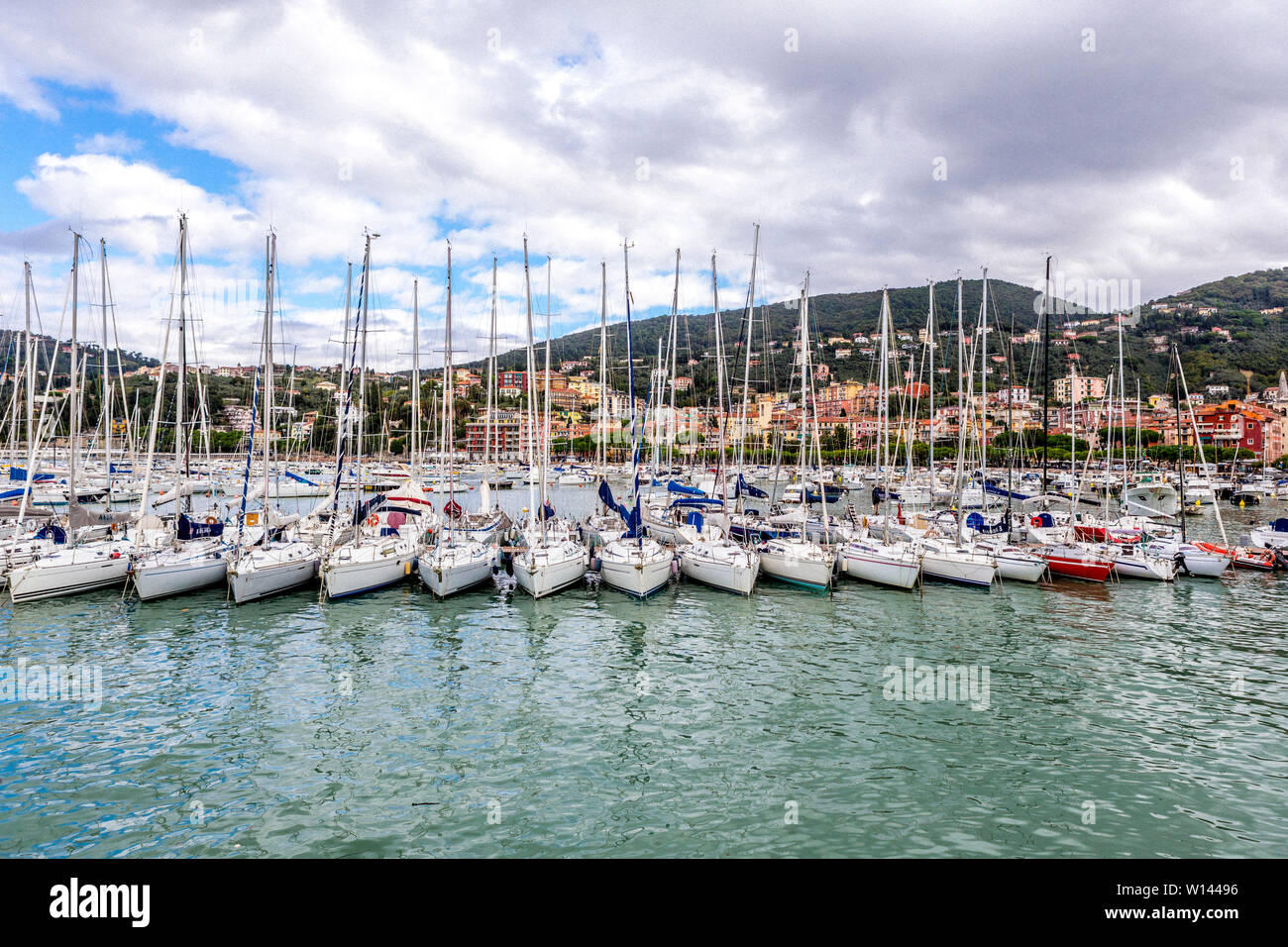 Segelboote ordentlich in einer Reihe in den Hafen und die Häuser auf den Hügeln, gegen bewölkten Himmel in Rapallo, Ligurien, Italien Stockfoto