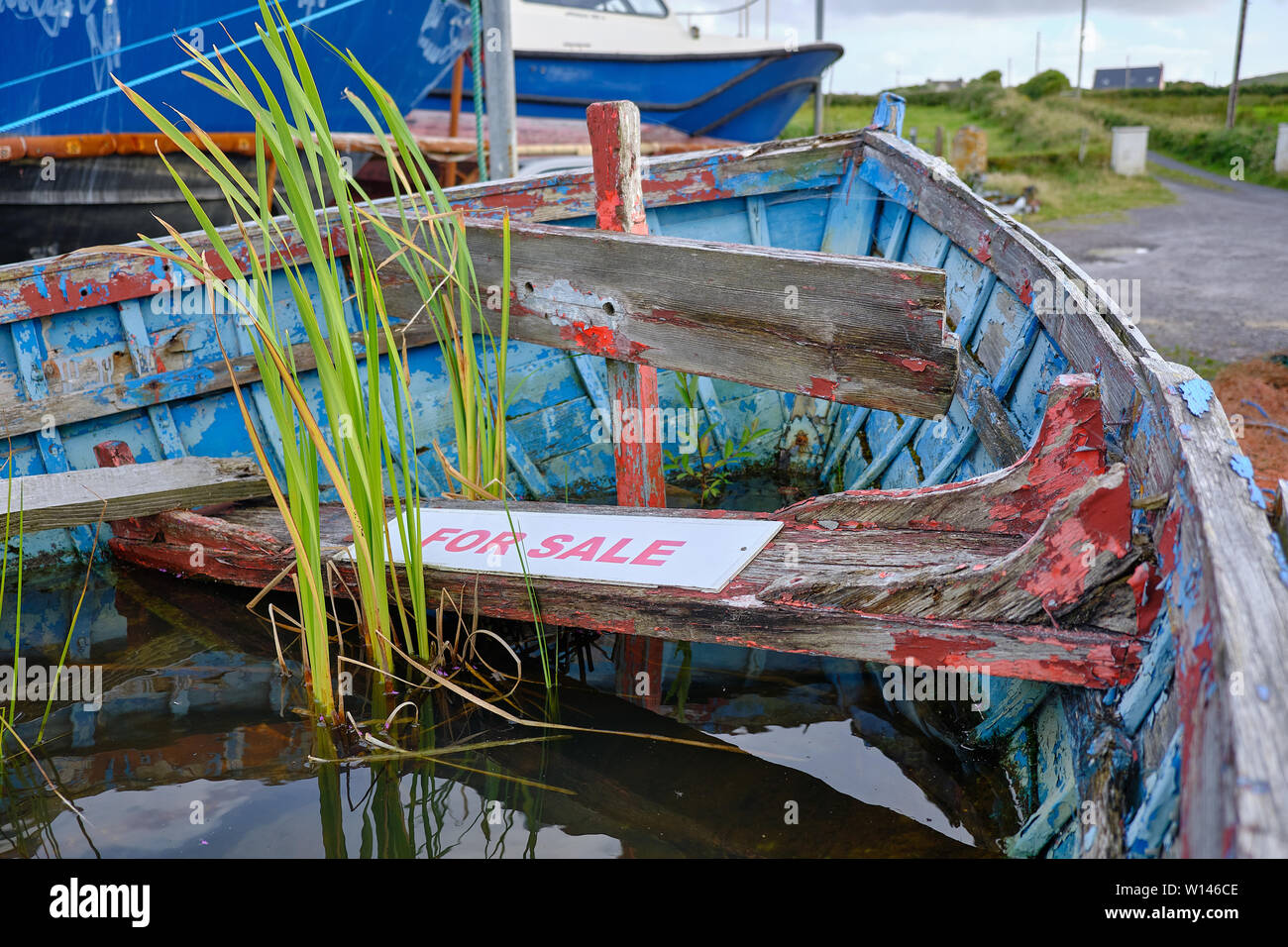 Nahaufnahme von innen Bogen von alten, verlassenen ruinierte Ruderboot, gefüllt mit Regenwasser mit Unkraut wächst, mit einem Schild "Zum Verkauf" auf morschen Sitzbank Stockfoto