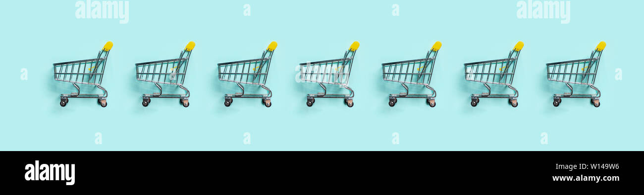 Warenkorb in der Zeile auf blauem Hintergrund. Minimalismus Stil. Spielzeug Trolley für einen Supermarkt. Top View oder flach. Sale, Discount, shopaholism Konzept. Konsumgesellschaft Trend. Stockfoto