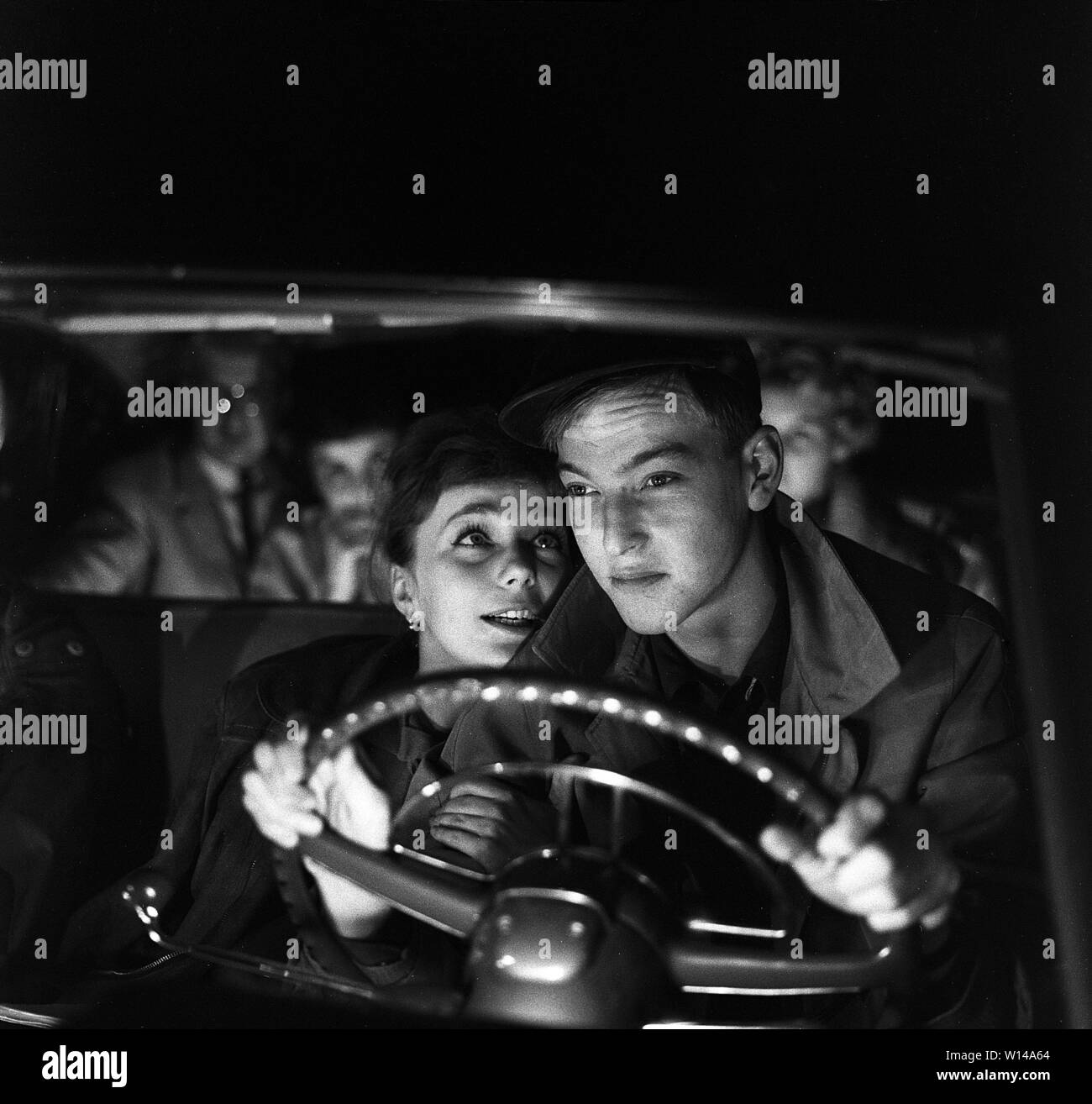 Das Fahren in den 1950er Jahren. Ein junges Paar im Fahrersitz. Er ist auf der Fahrt in die dunkle Nacht und seine Augen sind auf den Verkehr konzentrieren. Sie ist mehr an ihm interessiert und sitzt so nahe zu ihm, als Sie kann. Schweden 1959. ref BV 100-2 Stockfoto