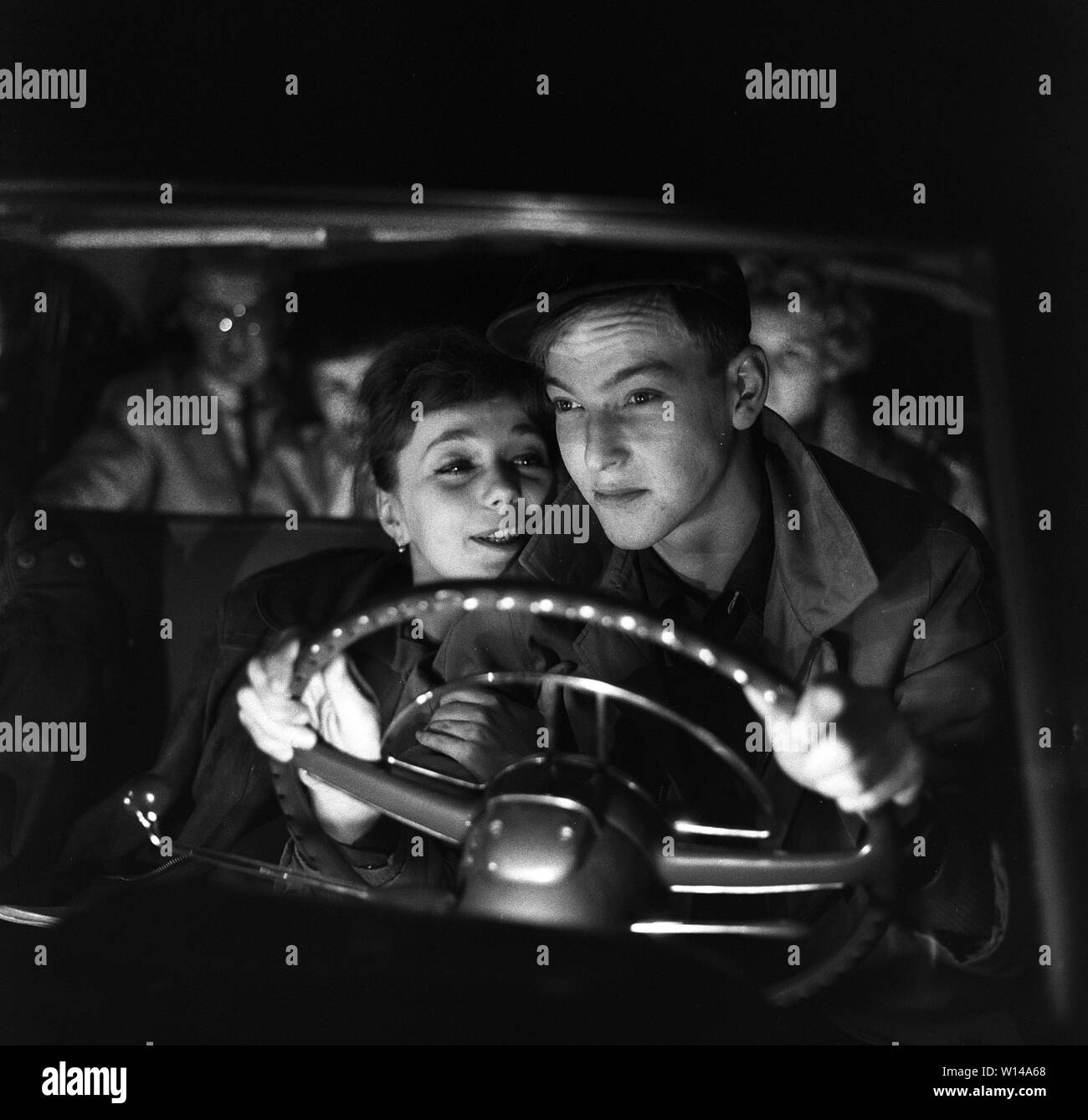 Das Fahren in den 1950er Jahren. Ein junges Paar im Fahrersitz. Er ist auf der Fahrt in die dunkle Nacht und seine Augen sind auf den Verkehr konzentrieren. Sie ist mehr an ihm interessiert und sitzt so nahe zu ihm, als Sie kann. Schweden 1959. ref BV 105-5 Stockfoto