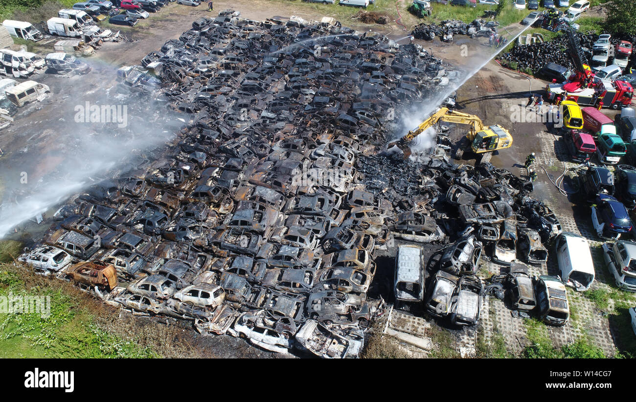 Duvendiek, Deutschland. 30. Juni, 2019. Feuerwehrmänner ein großes Feuer  löschen auf einem Schrottplatz in der Nähe von Niepars (Landkreis  Vorpommern-Rügen) in der Nähe von Stralsund (Foto mit Drone). Rund 500  Autowracks und