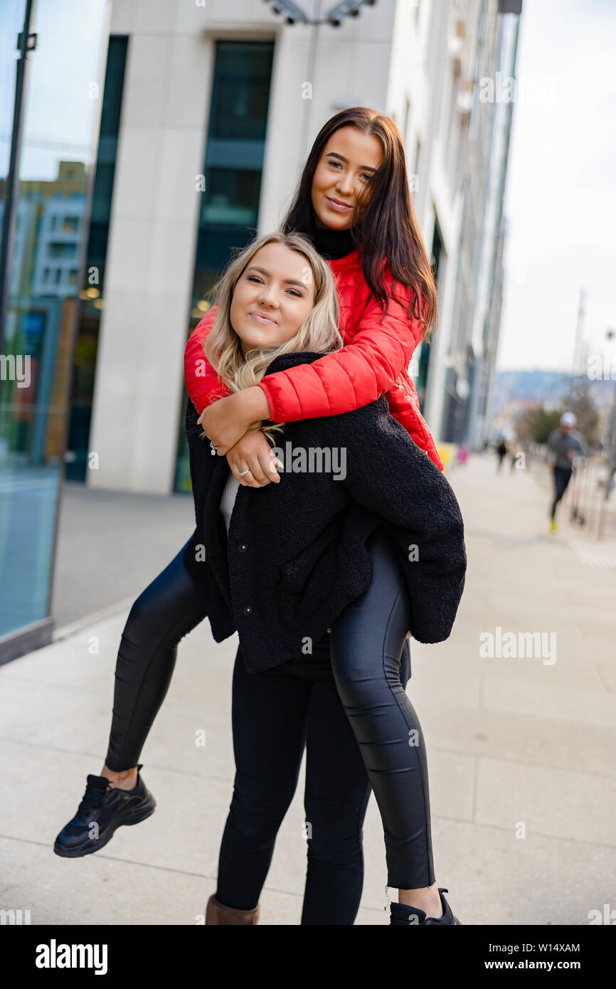 Lächelnd weibliche Freunde Spaß und Huckepack in der Stadt Umgebung Stockfoto