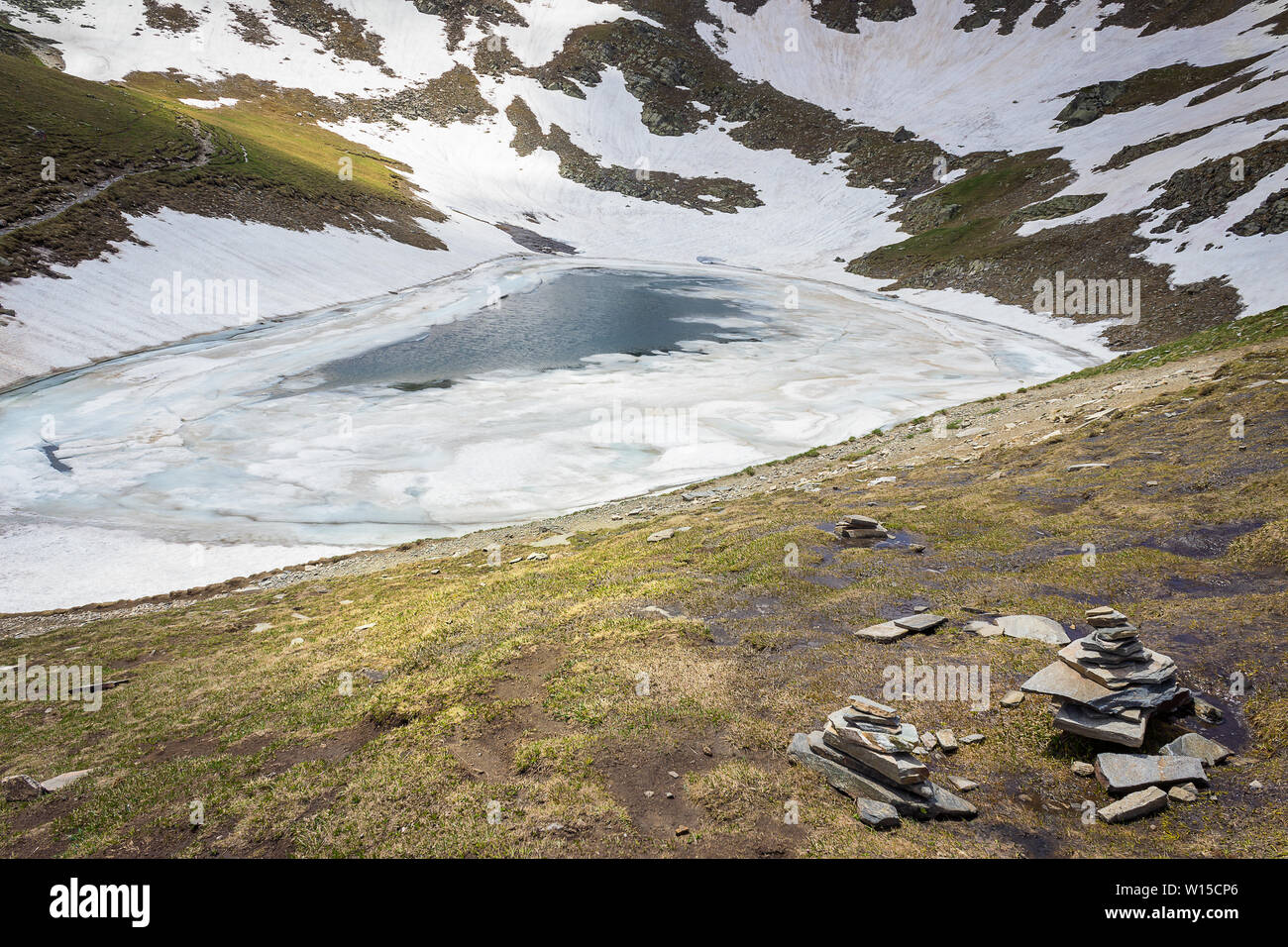 Die Träne See, einer der berühmten sieben Rila Seen, die von bunten gebrochene Eis und Schnee bedeckt, Vordergrund Haufen von Felsen und sonnenbeschienenen Hochländer Stockfoto