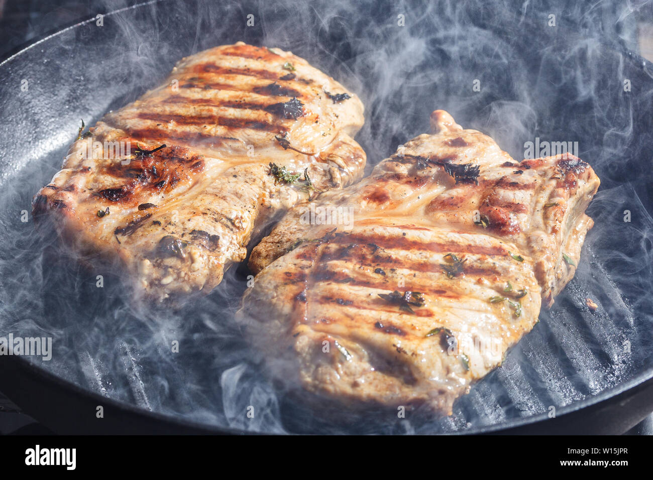 Rauch und Dampf Aufstieg aus einem Schwein Steak auf dem Grill Pfanne Stockfoto