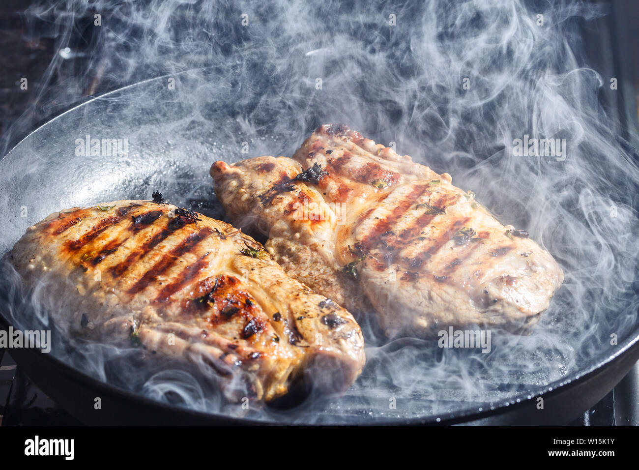 Rauch und Dampf Aufstieg aus einem Schwein Steak auf dem Grill Pfanne Stockfoto