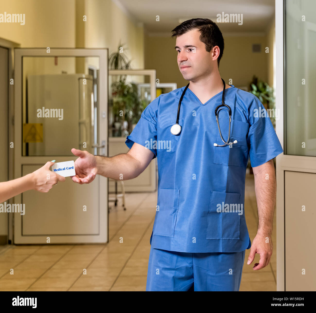 Mittleren Alters, kaukasischen weißen, männlichen Arzt in Scrubs mit Stethoskop akzeptieren Medical Card, verschwommenes Krankenhaus Flur im Hintergrund Stockfoto
