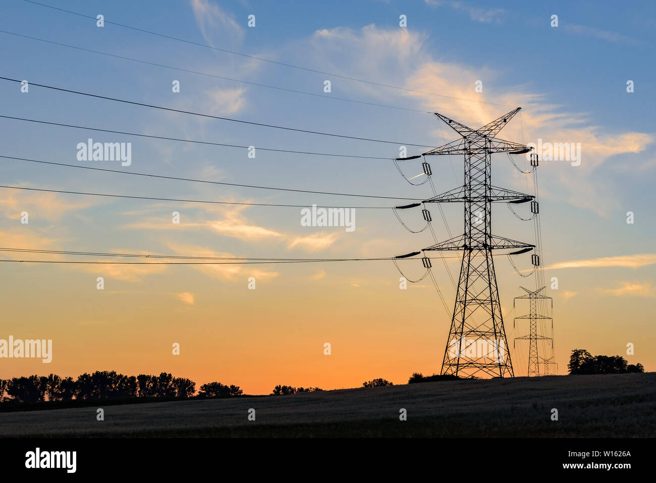 Strommasten und Hochspannungsleitungen bei Sonnenuntergang Stockfoto