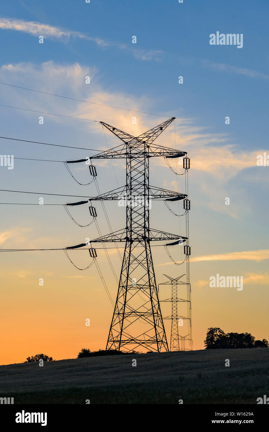 Strommasten und Hochspannungsleitungen bei Sonnenuntergang Stockfoto